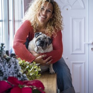 Cheerful dog owner beautiful adult female at home hugging her pug with love and tenderly - concept of people and animals pet therapy - adorable little domestic dog lifestyle and woman